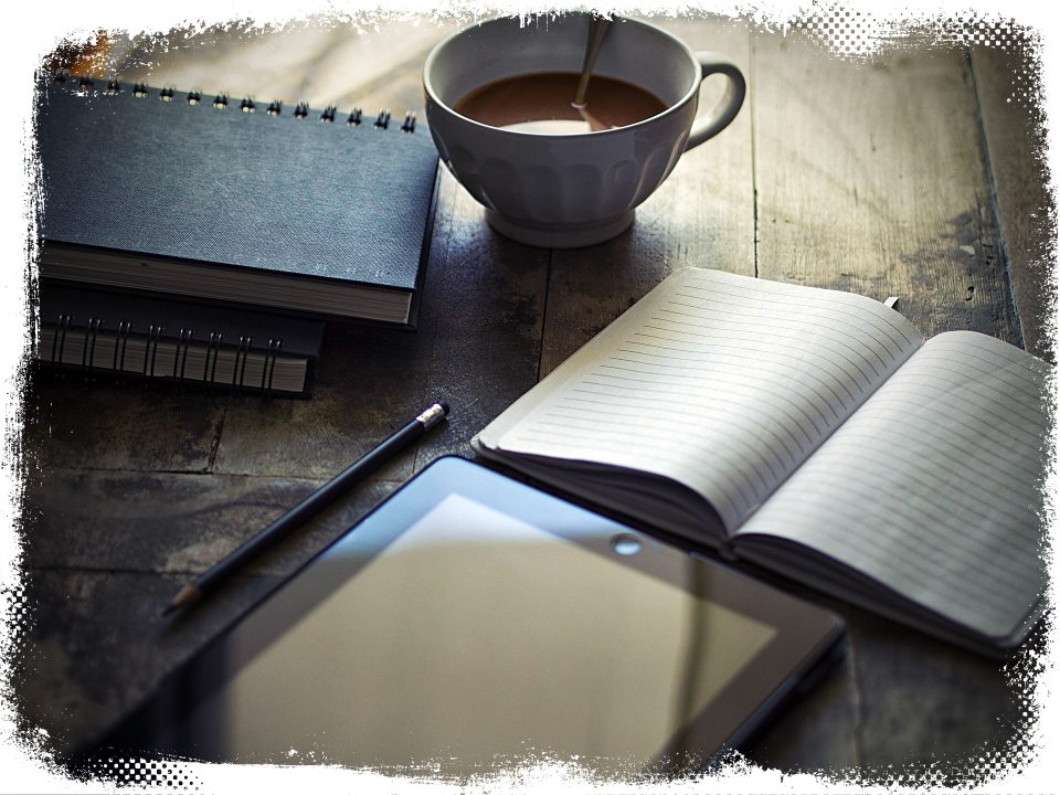 A colour photograph of a distressed wooden table on which is: a white cup half filled with coffee; an e-reader; a pencil with eraser; three spiral-bound, black-covered notebooks, one open.